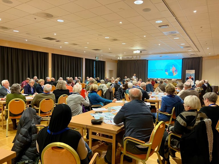 Konferansesal der det sitter mange mennesker og følger med på en presentasjon