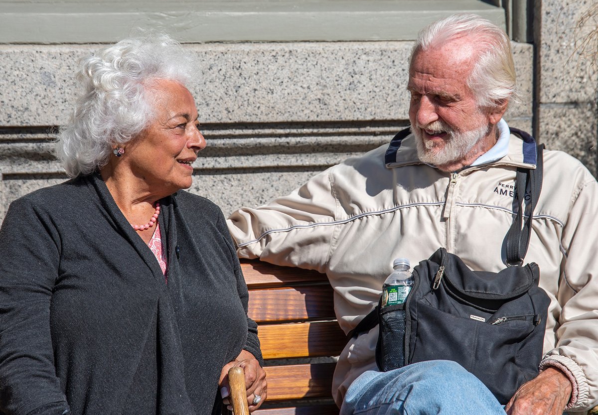 Et eldre par sitter på en benk og smiler til hverandre