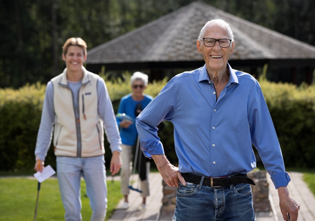 En eldre mann står fremst i bildet og smiler. Bak han står en yngre