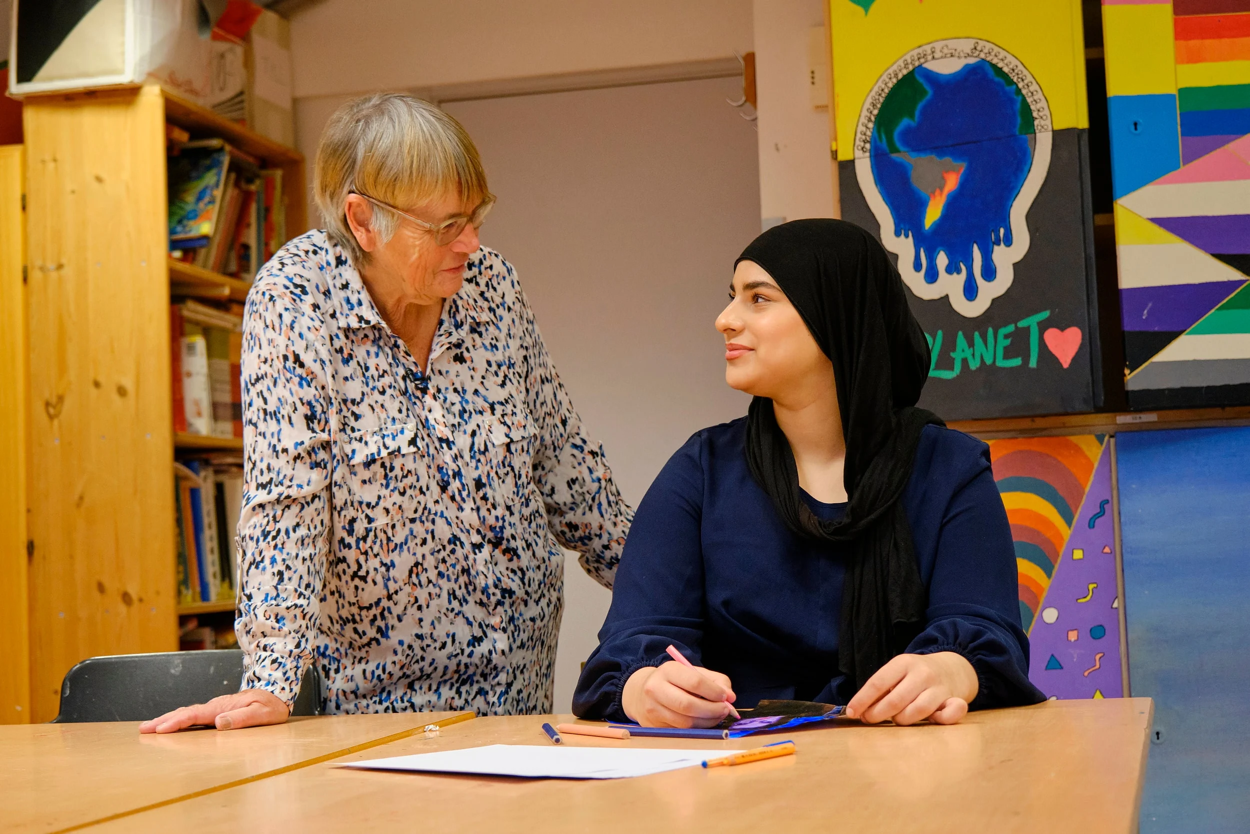 Eldre dame står ved siden av pulten til en ungdom