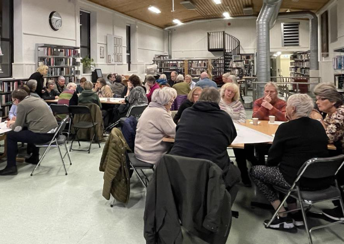 Flere mennesker sitter rundt flere bord og diskuterer.