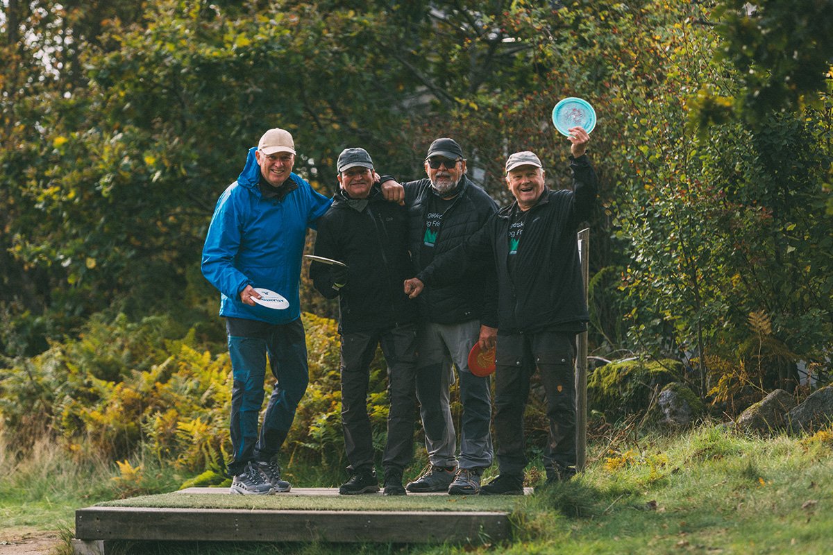 Fire eldre menn står side ved utendørs med en frisbee i hånda. 