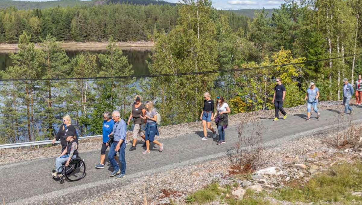 Flere mennesker går tur på en grusvei - eldre, yngre og en i rullestol. 