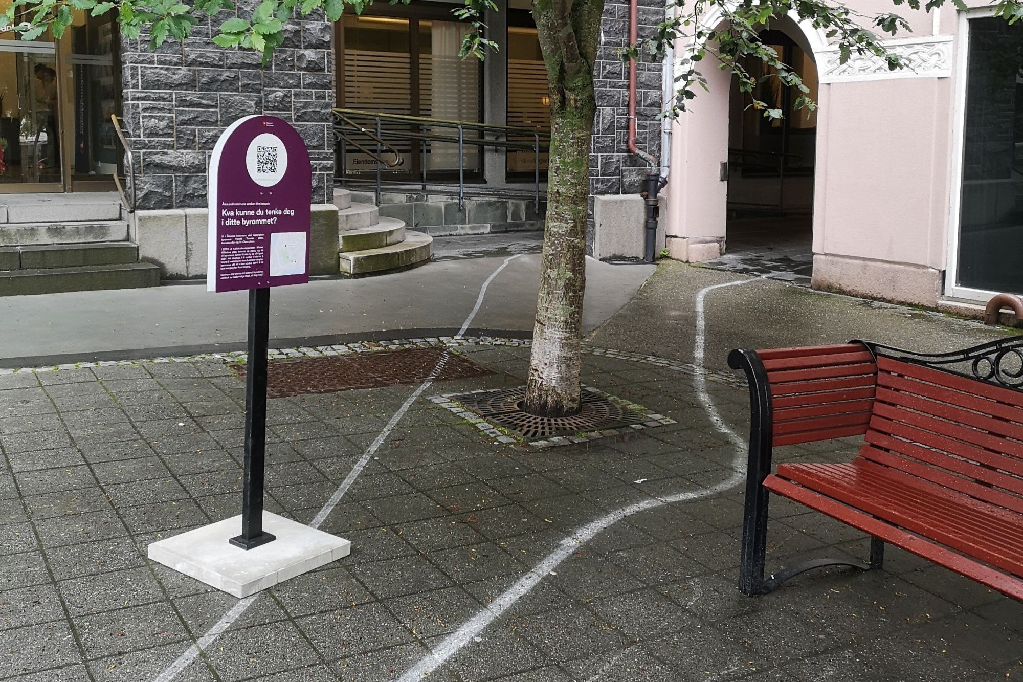 Et skilt med QR kode og en benk i et bymiljø