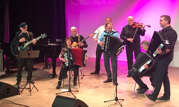 Et band med trekkspill, fele og gitar står på en scene og spiller
