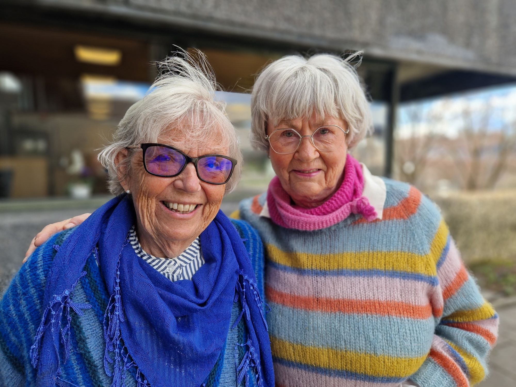 To eldre damer står ved siden av hverandre og smiler 
