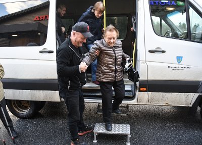 Eldre dame får hjelp ut av en minibuss