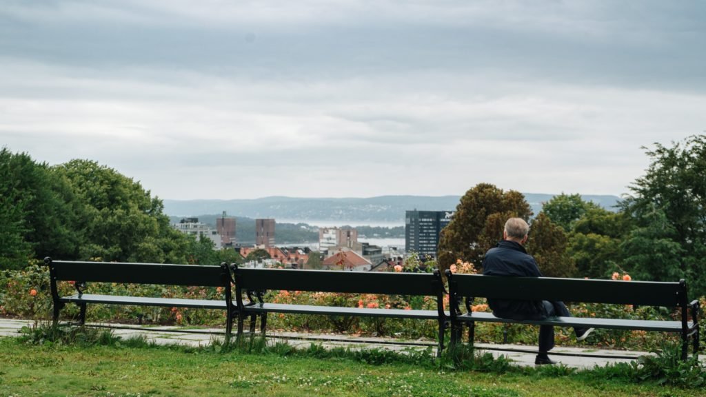 Eldre mann sitter på en benk å ser utover et Oslo