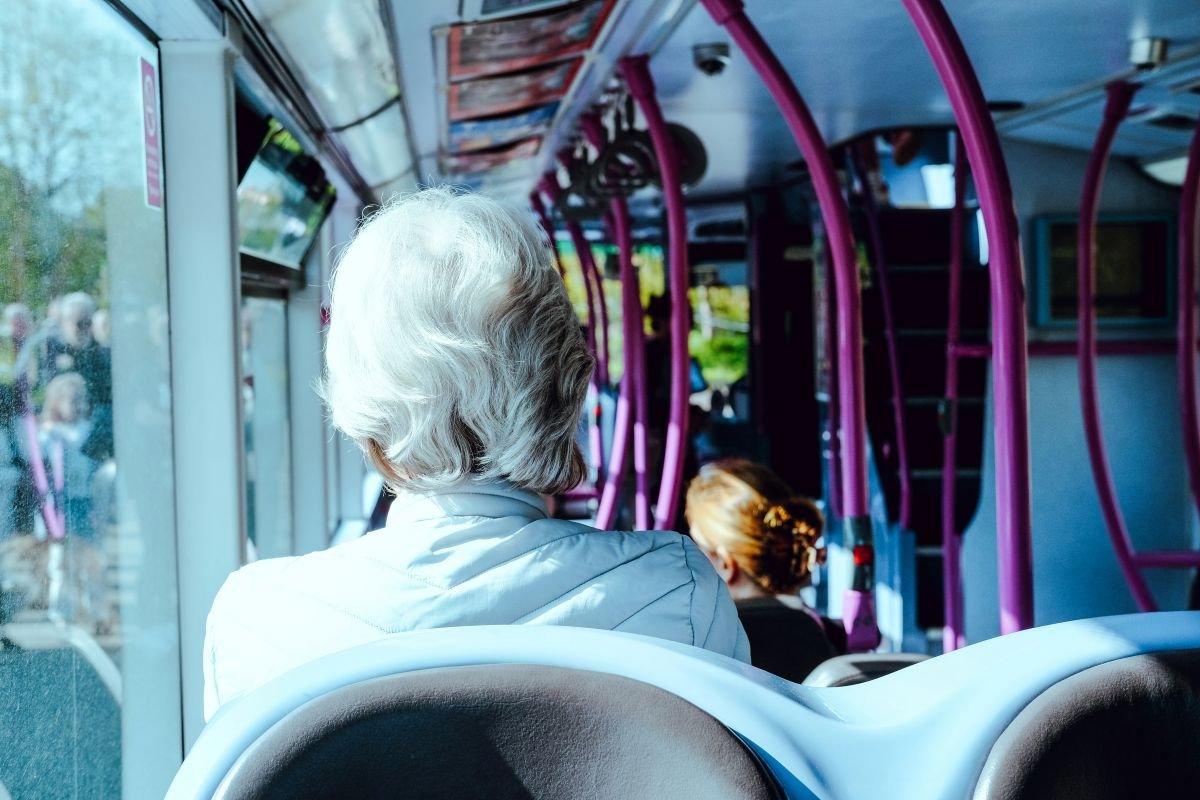 Eldre dame sitter på bussen med ryggen til