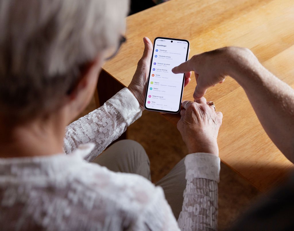 Eldre dame holder en smarttelefon som en annen peker ned på