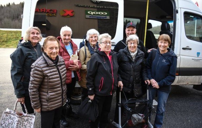 eldre mennesker stående i en gruppe foran en minibuss