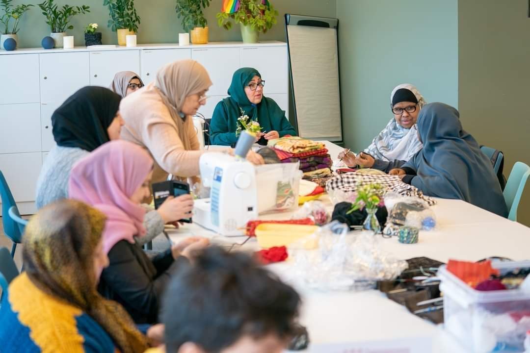 Flere damer sitter rundt et bord å syr og strikker